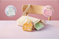 Pastel kawaii mini spiral notebooks with die-cut shaped tops featuring cute bear and blob characters. The orange, pink, blue, and green pocket journals feature motivational quotes like 'Heal every day' and 'Don't Be Sad', and are arranged playfully around a beige canvas crossbody bag on a pastel desk setting, perfect for aesthetic stationery collections.